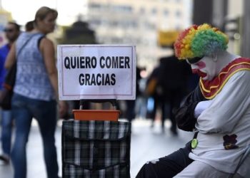 Rayito, a beggar dressed as a clown sits next to a placard reading "I want to eat, thank you" in Gran Via street, in the centre of Madrid, on October 28, 2014.   AFP PHOTO/ GERARD JULIEN        (Photo credit should read GERARD JULIEN/AFP/Getty Images)